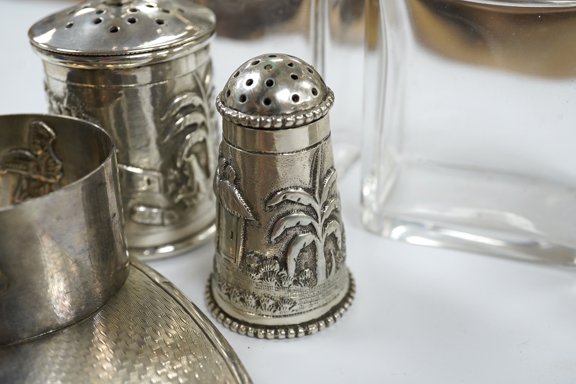 Small silver including a napkin ring, hand mirror and two mounted glass toilet jars, together with three Indian white metal condiments and a French white metal wine taster. Condition - poor to fair